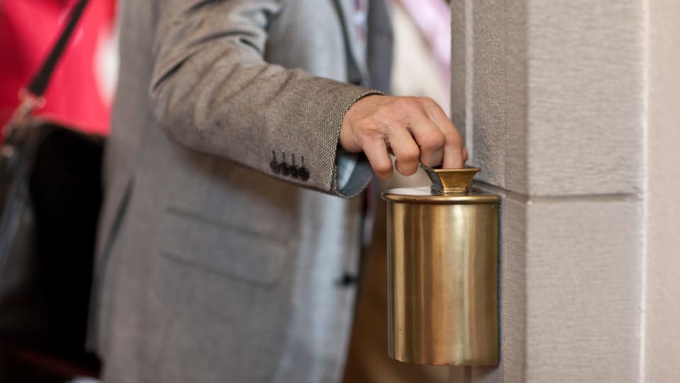 Ein Mann wirft beim Heraustreten aus der Kirche Geld mit seiner Hand in einen Behälter. 