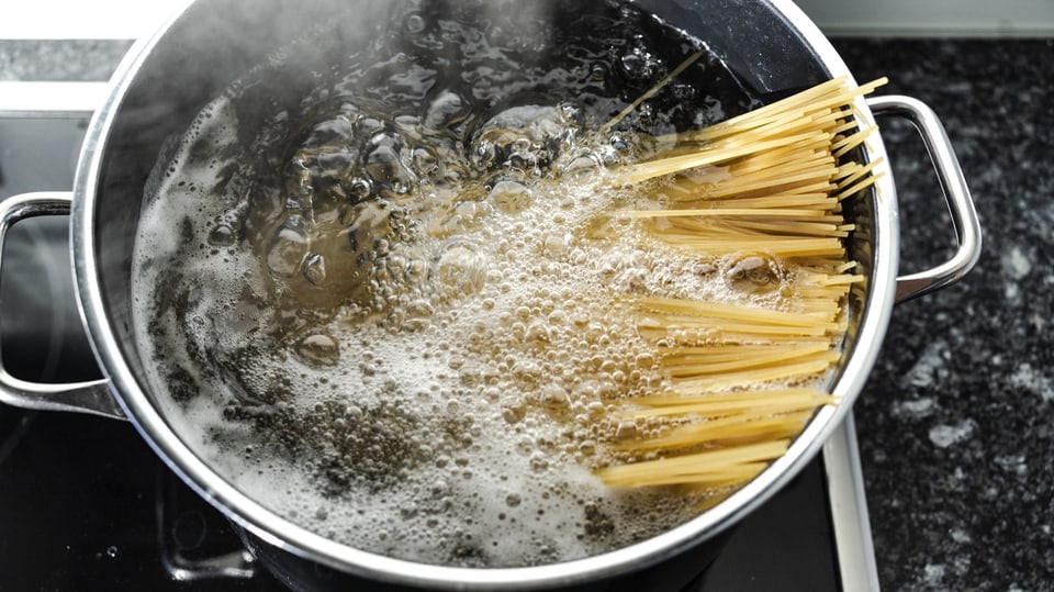 Ein Teller mit Spaghetti wird von einer Hand ins Bild gereicht, eine andere nimmt Pasta mit einer Gabel vom Teller