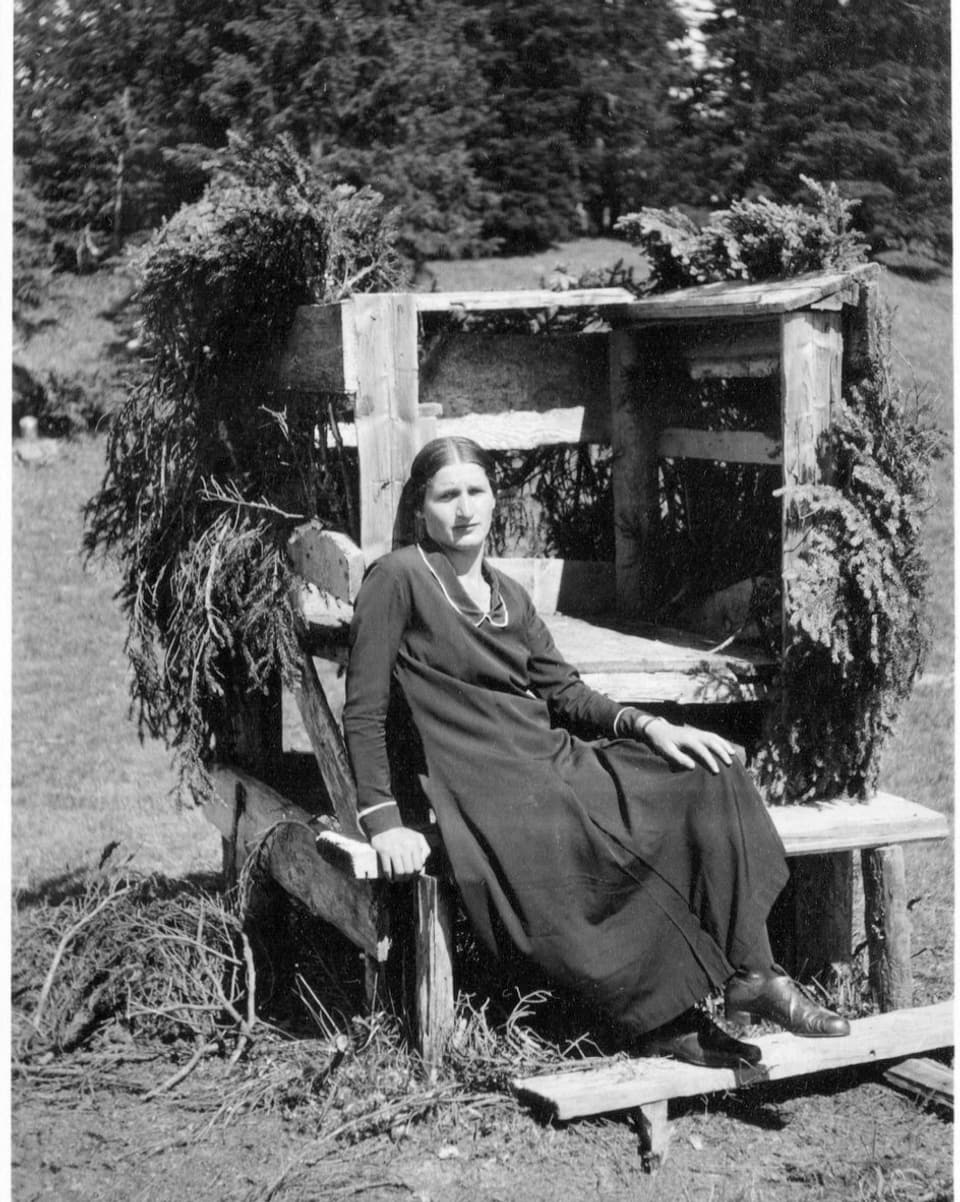 Schwarzweiss-Foto einer Frau auf Holzbank vor dem Wald.