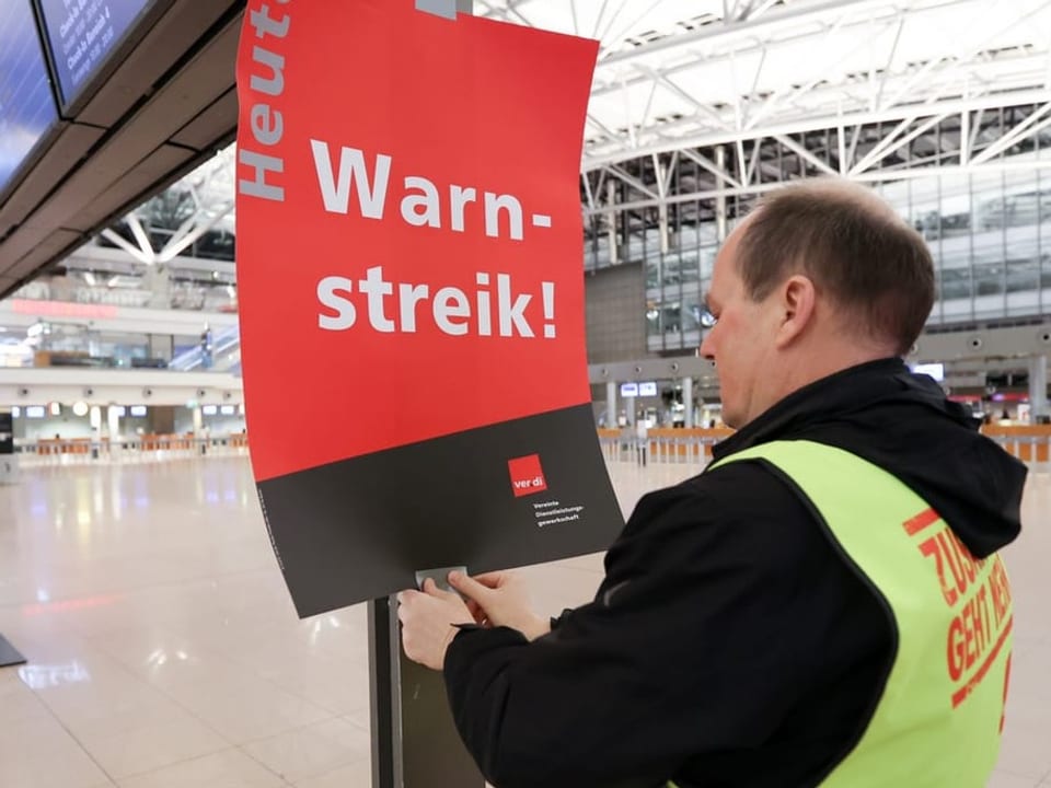 Ein Mann hängt ein Plakat auf mit der Aufschrift «Warnstreik!»