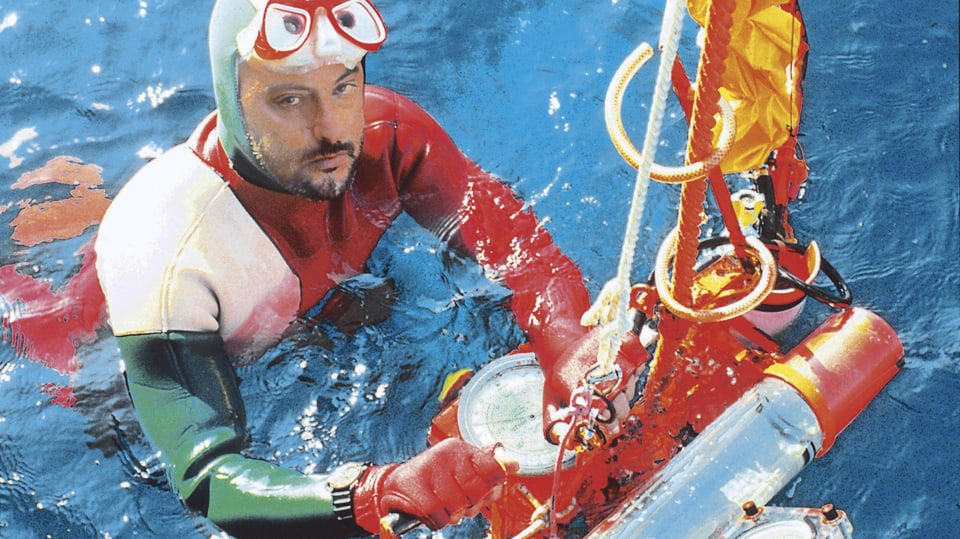 Ein Mann mit Taucheranzug und Taucherbrille auf der Stirn schwimmt im Wasser und hält sich an einer Joje fest.