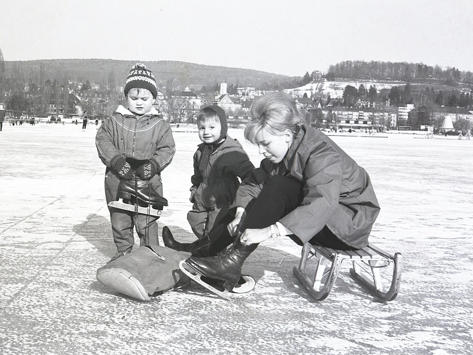 Ein Schwarz-Weiss Bild aus 1964 mit einer Frau und zwei Kinder auf einem gefrorenem See. 