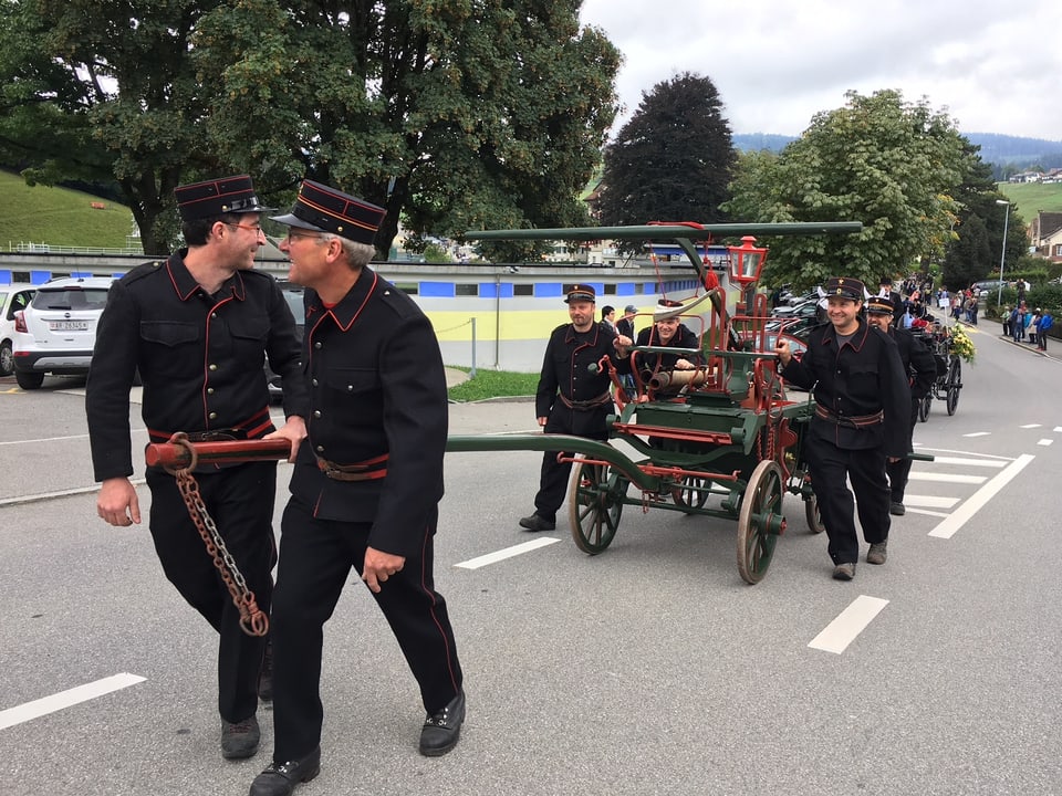 Männer in schwarzen Kostümen ziehen Leiterwagen