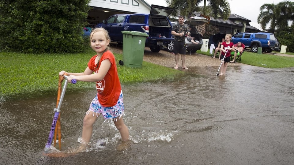 Mädchen mit Trotinett spielt vor einem überfluteten Haus.