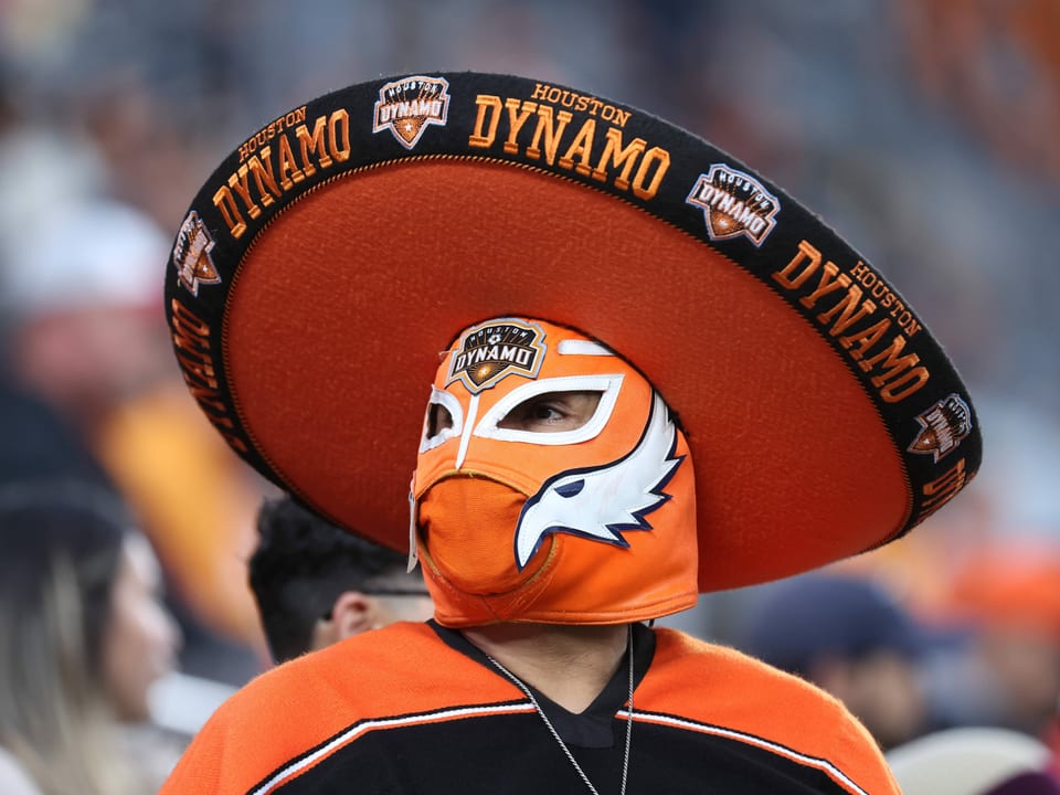 Orange-schwarz gekleideter Fan mit Maske und Sombrero.
