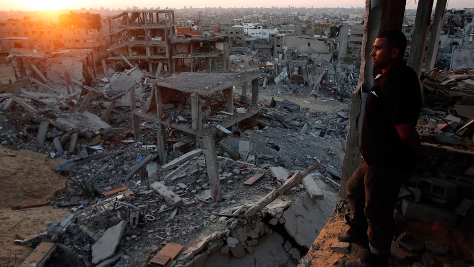 Mann schaut aus einem Haus auf die zerstörte Stadt.
