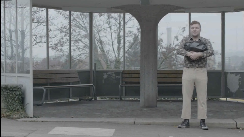 Ein Posträuber steht mit einem Abfallsack, gefüllt mit Tausendernoten an der Busstation. (Filmausschnitt)