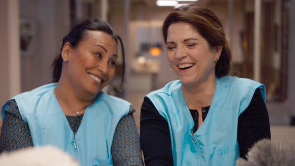 Zwei Frauen in blauen Kitteln lachen gemeinsam.