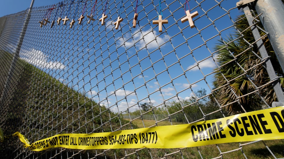 Zaun vor der Schule in Florida. Daran sind ein Absperrband und Holzkreuze befestigt.