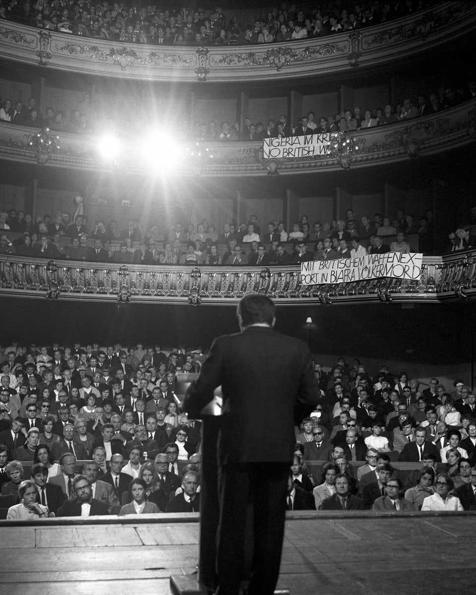 Ein Mann steht allein auf einer Bühne und blickt in den voll besetzten Saal.