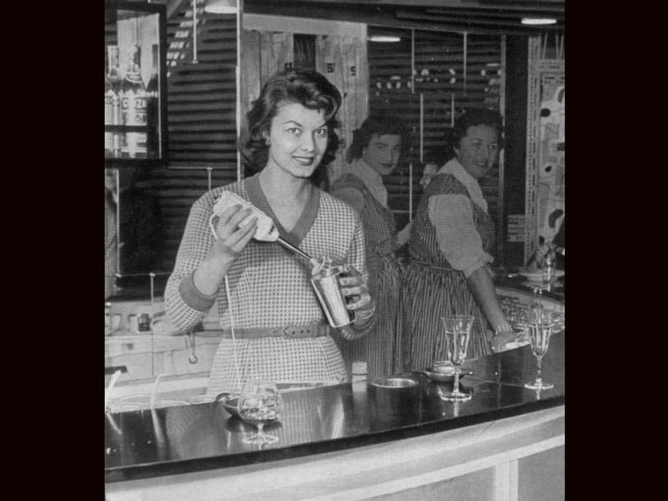 Schöne Frau hinter einer Bar mixt mit Stabmixer einen Drink.