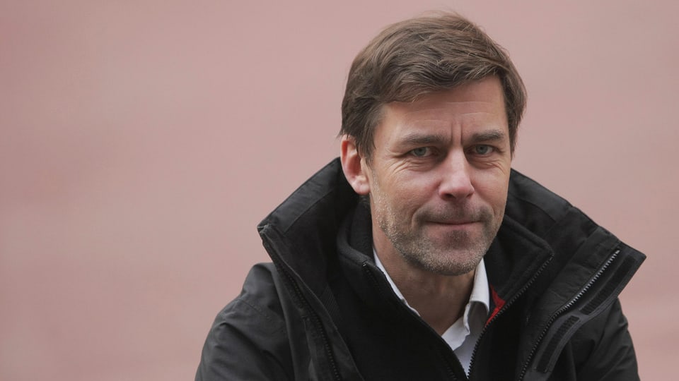 Peter Stamm mit einer dunklen Jacke vor einer hellen, rötlichen Wand