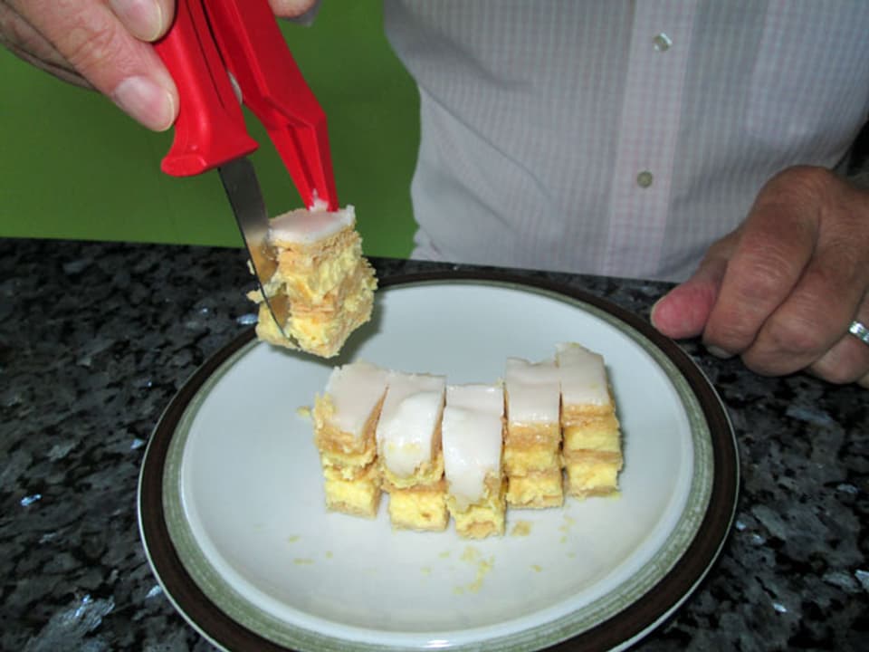 Mann zerteilt Crèmeschnitte einhändig mit einem speziellen Schneidegerät.