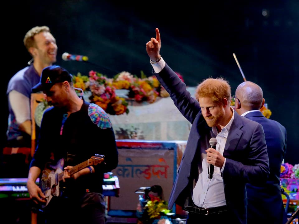 Zusammen mit Chris Martin (hinten links) und Guy Berryman (vorne links) steht Prinz Harry (rechts) auf der Bühne.