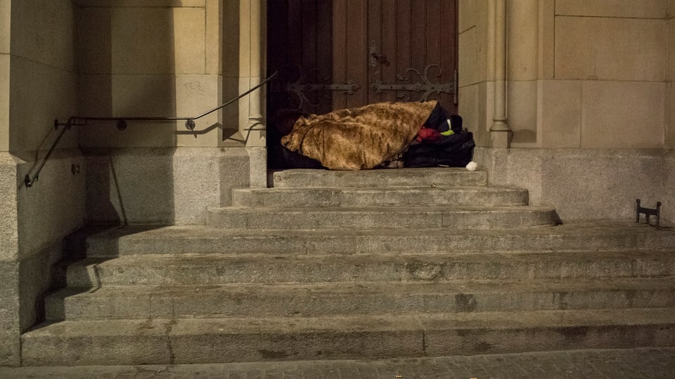 Auf einer Treppe in der Zürcher Innenstadt liegt ein Obdachloser dick eingepackt in Decken.