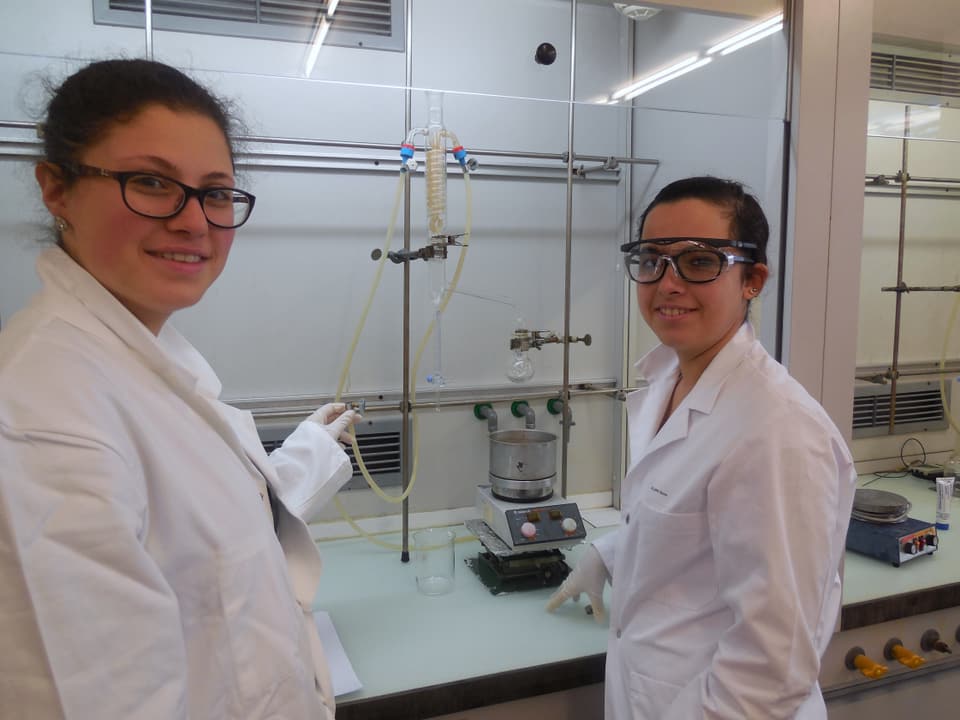 Zwei junge Frauen stehen mit weissen Kitteln in einem Labor.