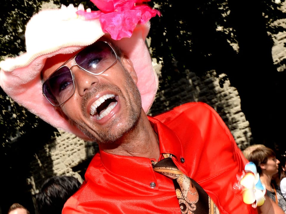 Ein Mann mit rosa Hut lacht in die Kamera.