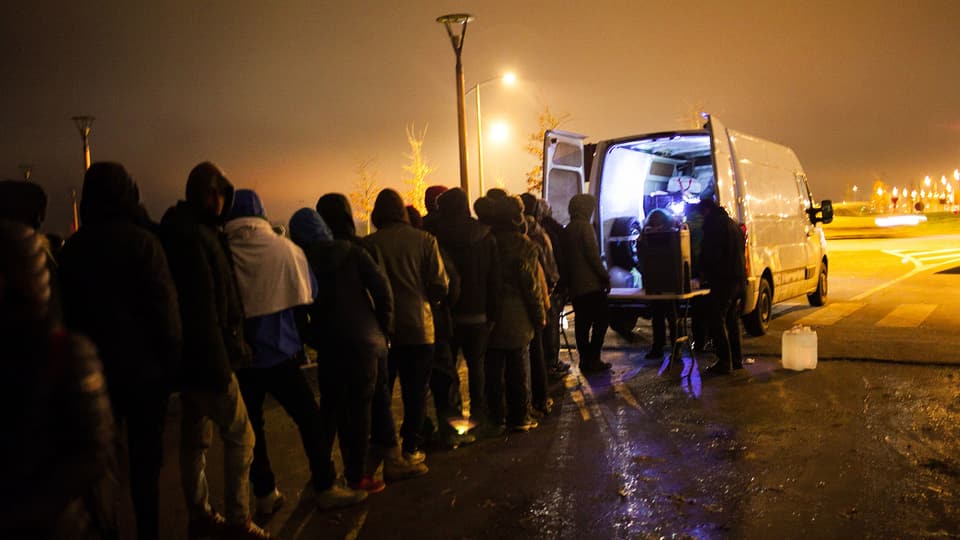 Leute stehen in der Nacht vor einem weissen Lieferwagen.