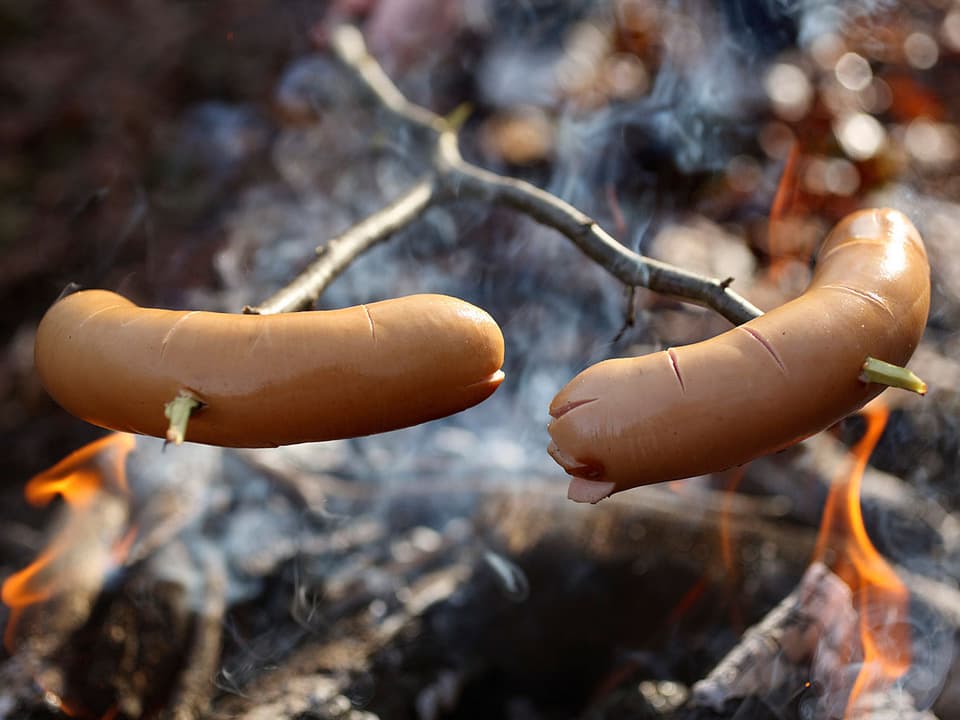 Zwei aufgespiesste Cervelats auf dem Feuer.