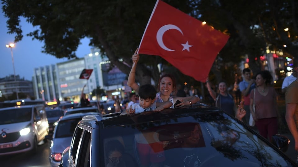 Eine Frau und ein Kind schauen oben aus einem Auto. Sie schwenkt eine türkische Fahne.