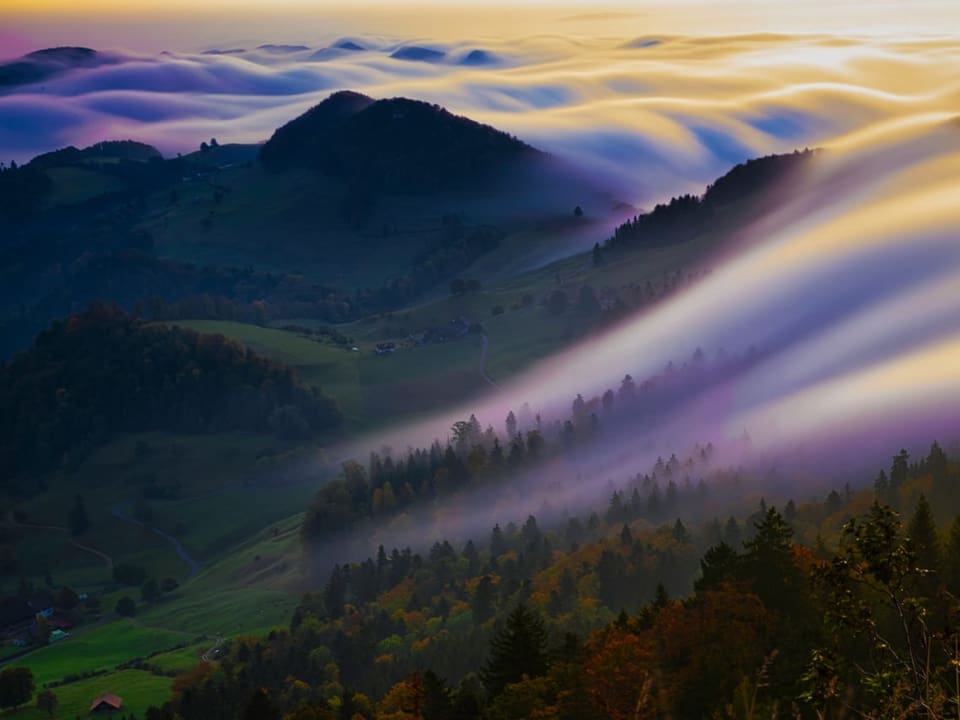 Hügelige Landschaft in der Morgendämmerung mit Nebel und einem Nebelfall. 