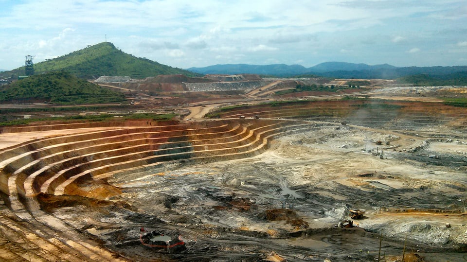 Symbolbild: Grossflächige Tagbau-Mine mit schwerem Gerät am Minenboden.