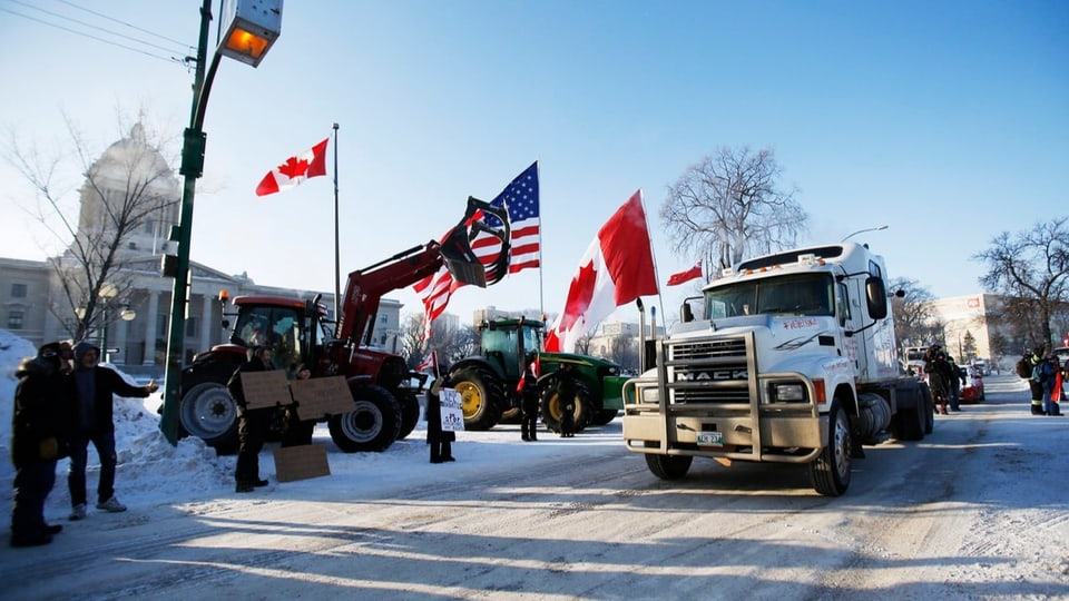 Lastwagen, Traktoren und anderes schweres Gerät im Schnee vor dem Parlamentsgebäude in Ottawa. Blauer Himmel.
