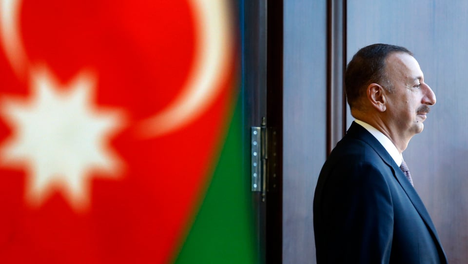 Präsident Alijev von der Seite vor einer Fahne Aserbaidschans.