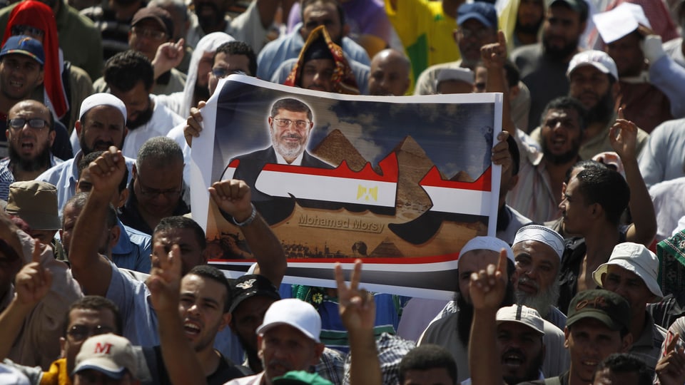 Muslimbrüder protestieren und halten ein Plakat von Mohammed Mursi hoch.