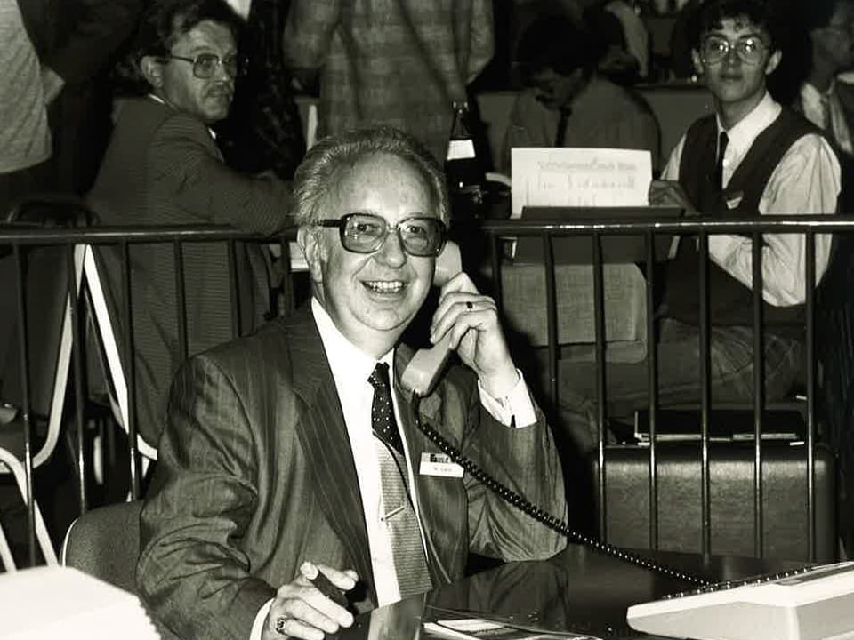 Auf der Schwarz-Weiss-Fotografie sitzt Martial Sialm an einem Pult und telefoniert.