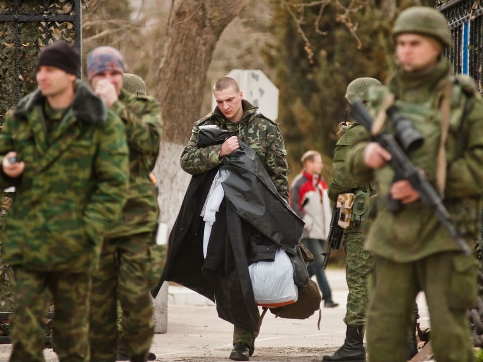 Soldaten ohne Erkennungszeichen auf der Krim, dahinter entwaffneter ukrainischer Soldat 