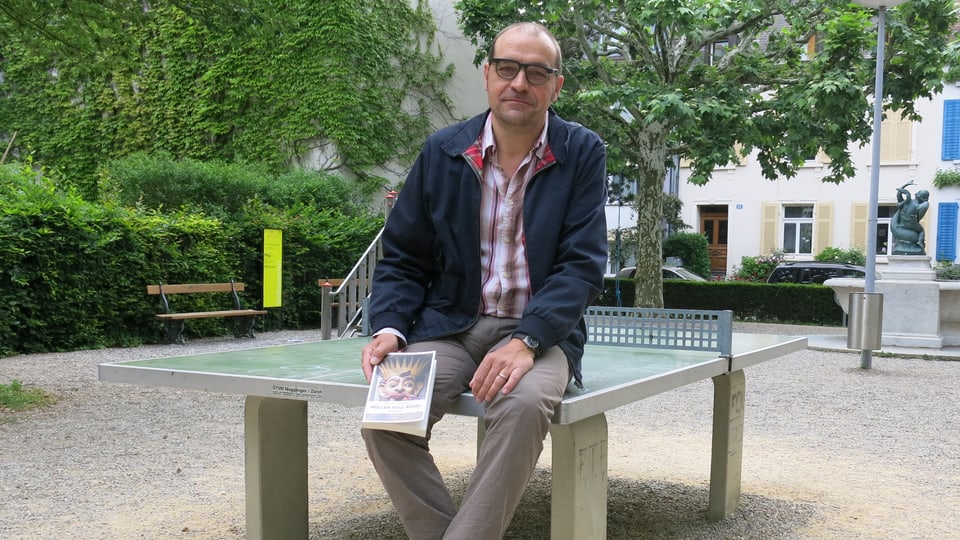 Raphael Zehnder auf einem Pingpong-Tisch mit seinem Buch