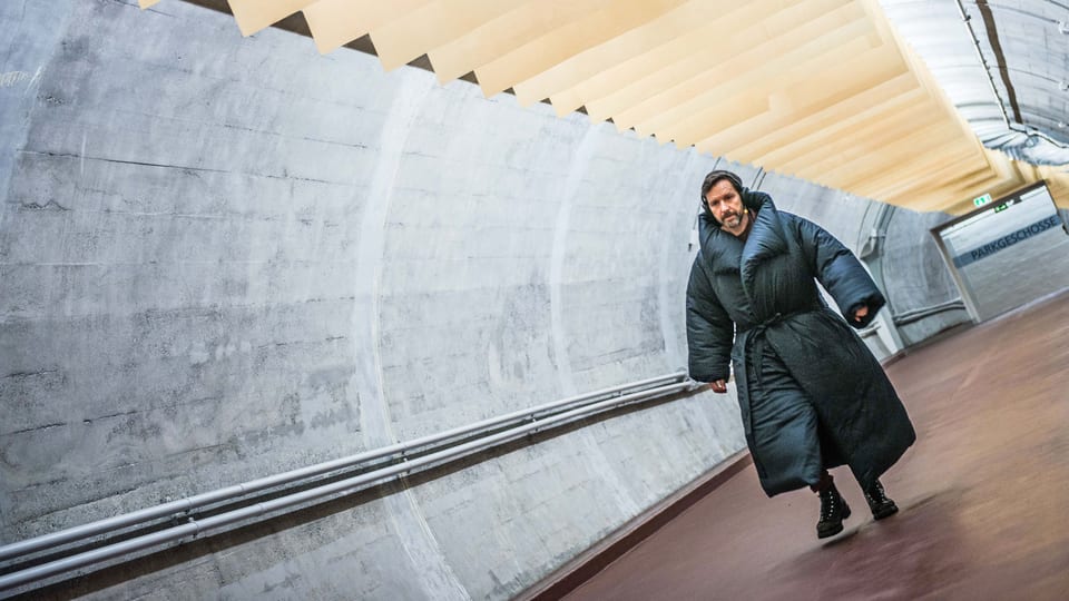 Ein Mann in dickem Mantel schreitet durch einen Tunnel. 