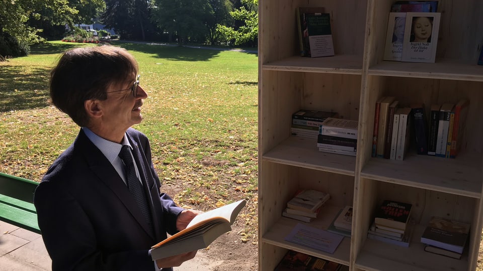 Ein Mann schaut in einen Bücherschrank in einem Park.
