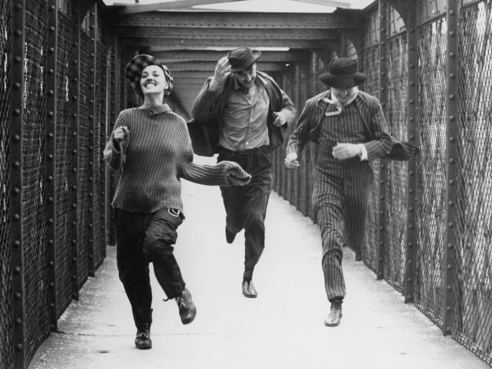 Eine Frau rennt lachend mit zwei Männern in Richtung Kamera.