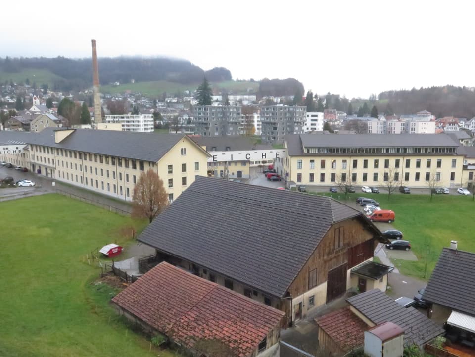 Blick auf ein Fabrikareal mit Bauernhof im Vordergrund