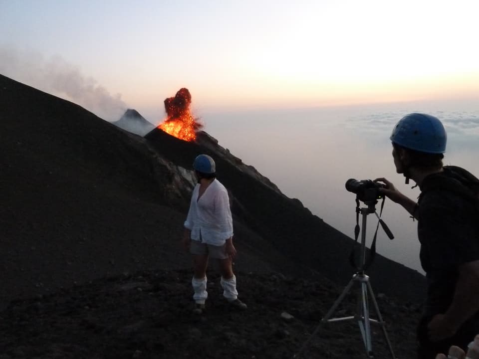 Zwei Menschen stehen vor eine Vulkan, der ausbricht