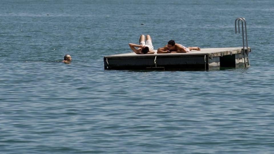 Menschen sonnen sich auf einem Floss im See.