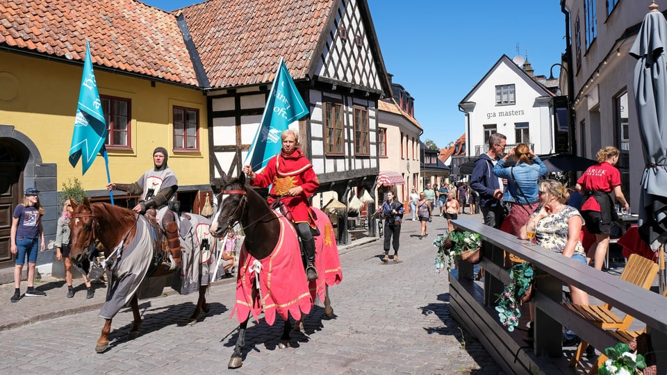Zwei Ritter auf Pferden mit Flaggen in einem Touristendorf in Schweden.