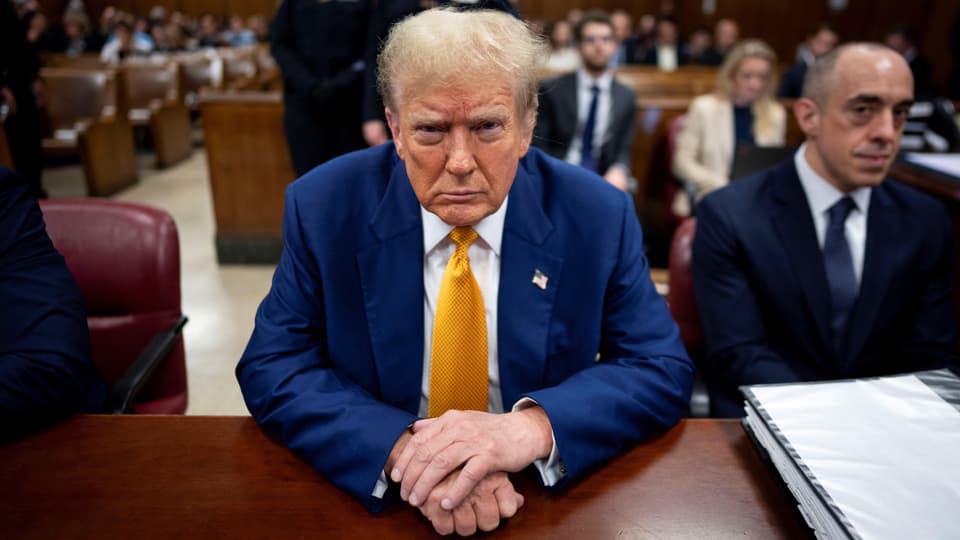 Donald Trump in blauem Anzug mit gelber Krawatte in einem Gerichtssaal.