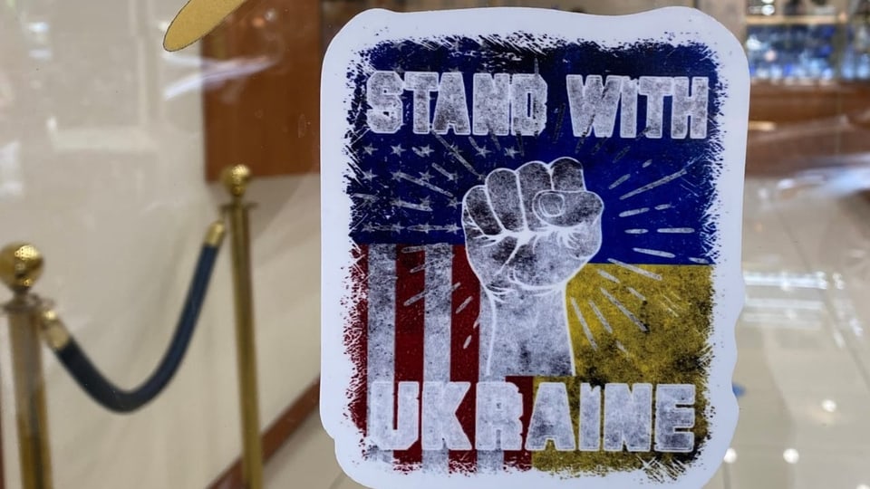 Ein Poster mit der Aufschrift: Stand with Ukraine klebt an einer Fensterscheibe.