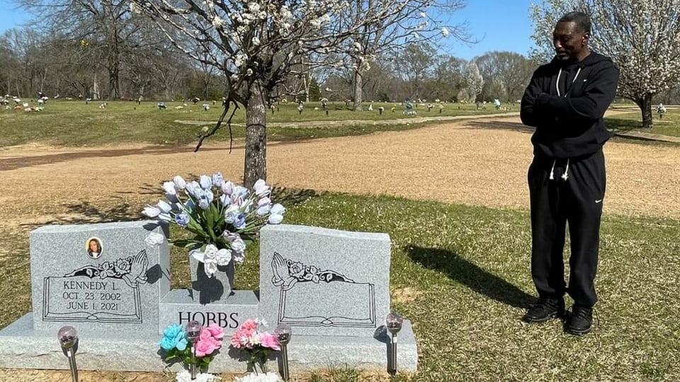 Mann stehet neben Grab mit Blumen
