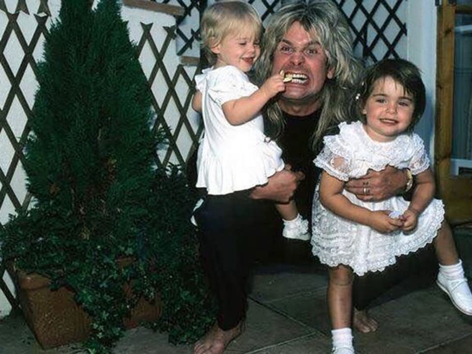 Ozzy Osbourne mit zwei seiner Töchter auf dem Arm.