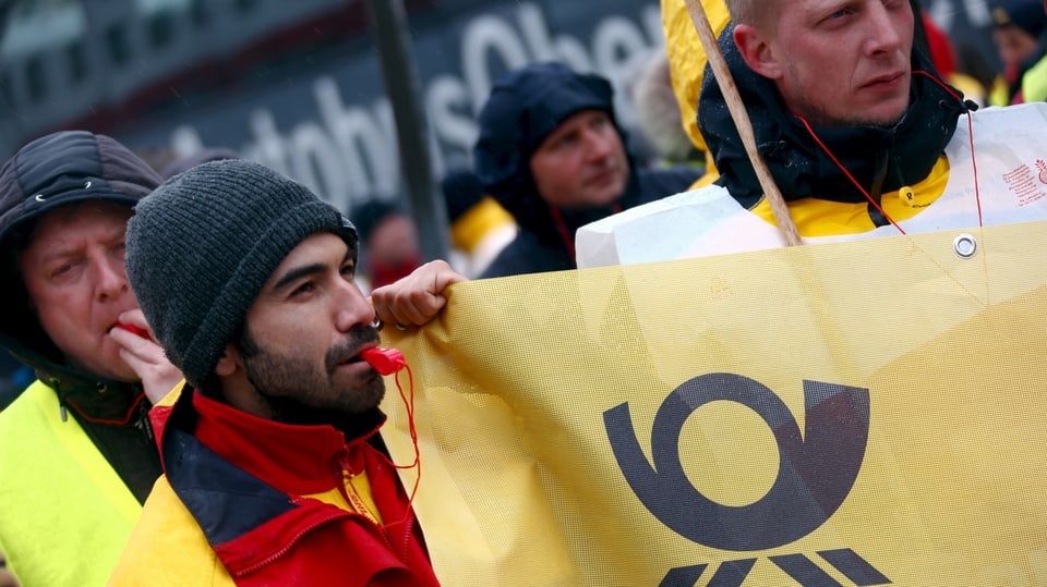 Pöstler beim Demonstrieren, einer hält ein gelbes Transparent mit dem Post-Logo vor sich hin