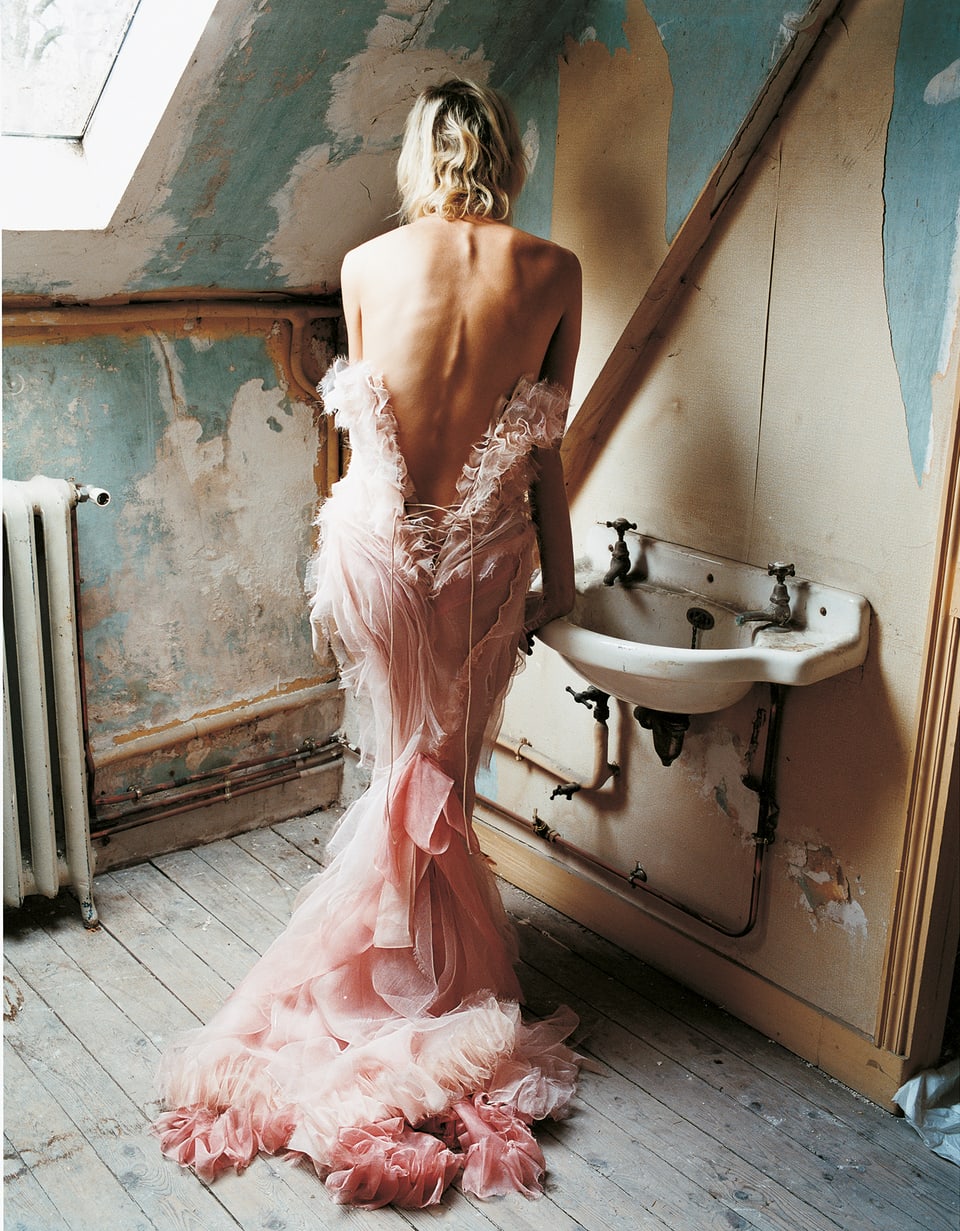 Ein rosafarbenes Kleid, abgelichtet in einem heruntergekommenen Dachzimmer. Das Model lehnt sich an ein altes Waschbecken, sie kehrt dem Fotografen ihren Rücken zu.