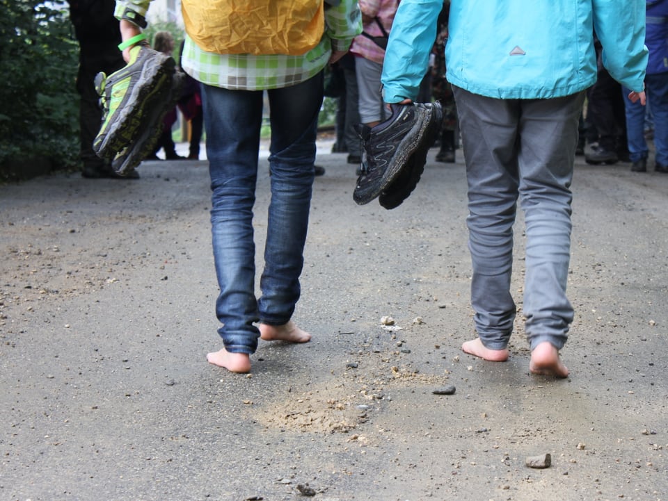 Zwei Mädchen gehen barfuss mit ihren Wanderschuhen in der Hand.
