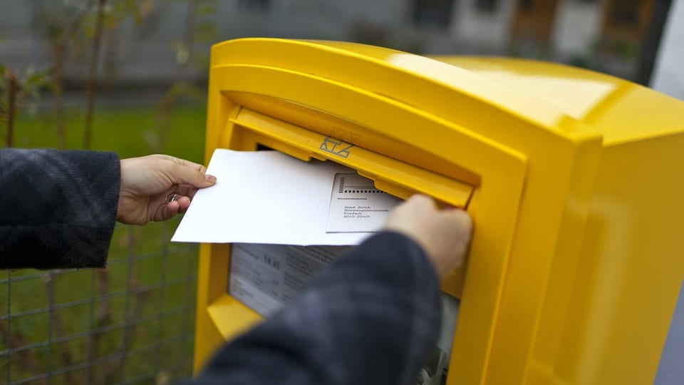 Frau wirft Stimmcouvert in einen Briefkasten.