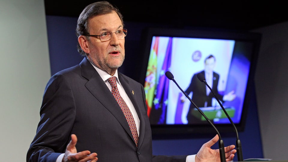 Spaniens Ministerpräsident Mariano Rajoy steht am Rendnerpult, dahinter ist er auf einem Bildschirm zu sehen.