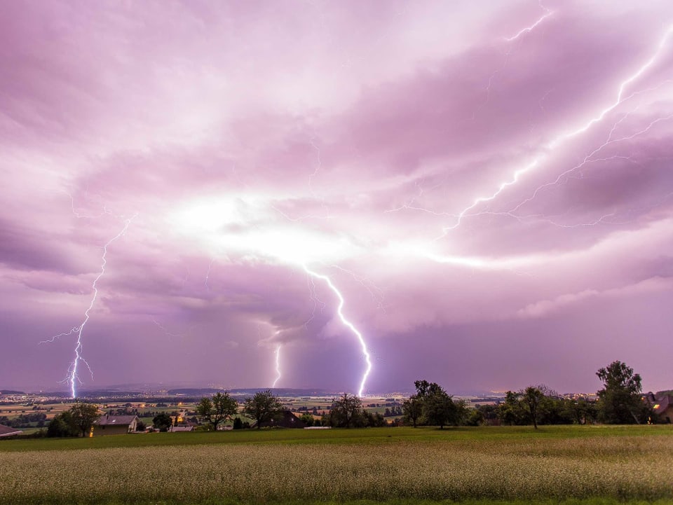 Aus einer violetten Wolke schiessen Blitze auf eine flache, ländliche gegend herab.