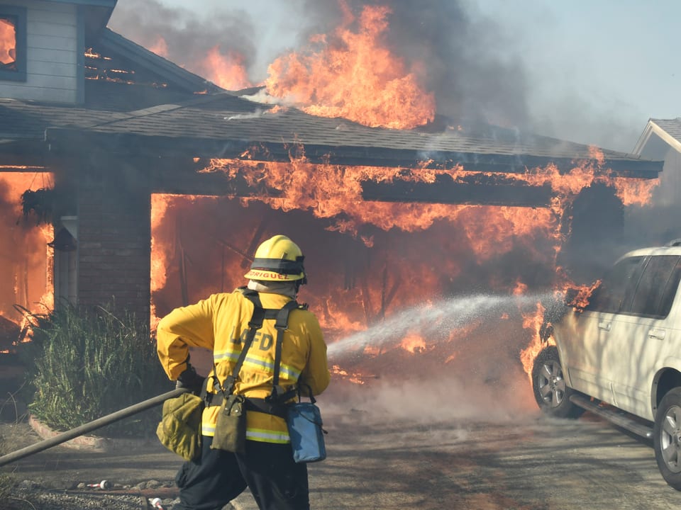Haus in Flammen, Feuerwehrmann versucht das Feuer zu bekämpfen. 
